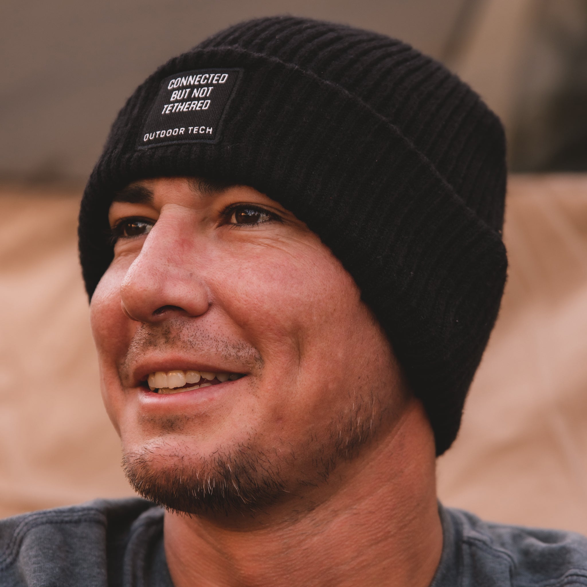 Image of a man smiling and wearing the Shred Beanie, with the path "Connected but not tethered" on the front.