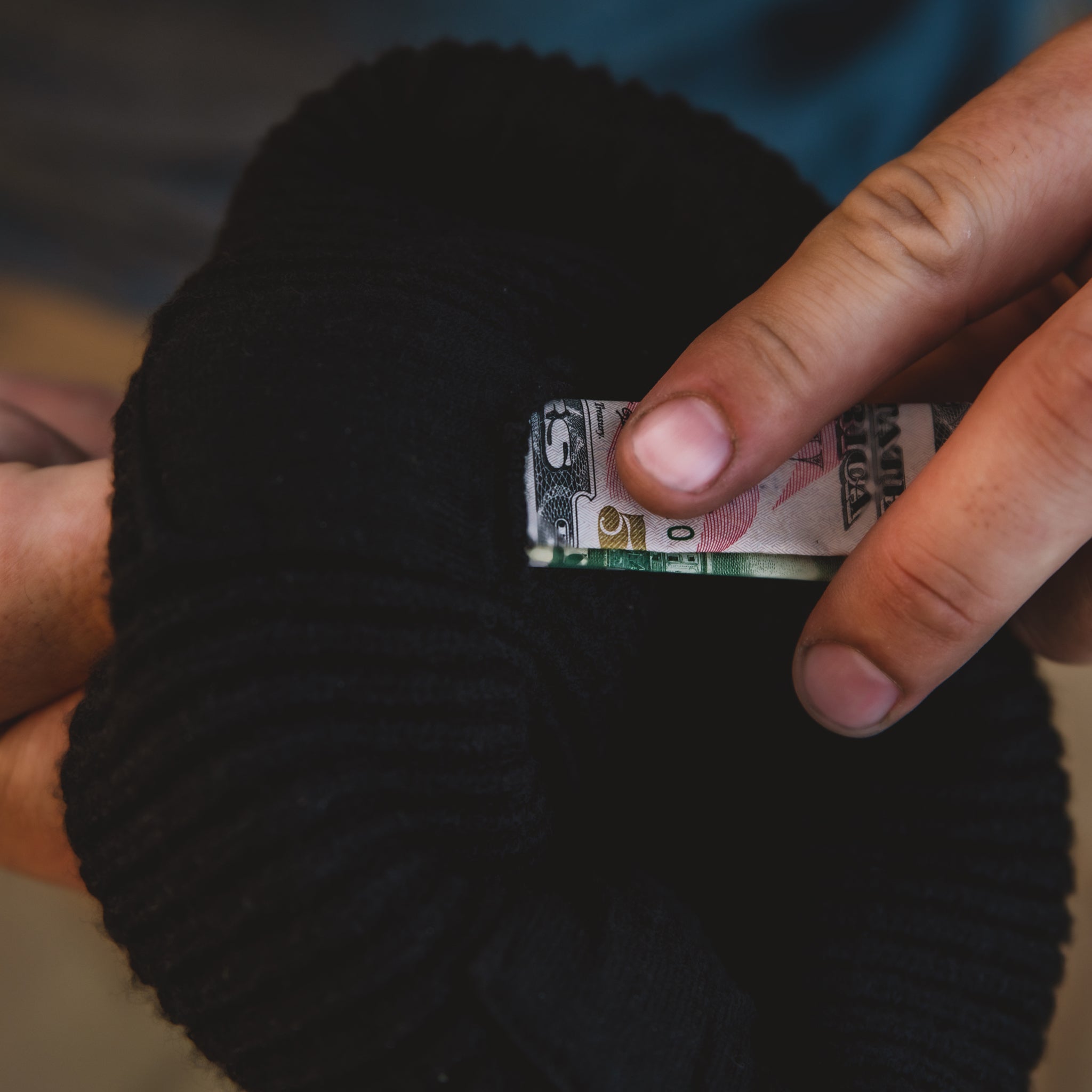 Close up view of someone putting a folded bill into the pocket on the Shred Beanie.